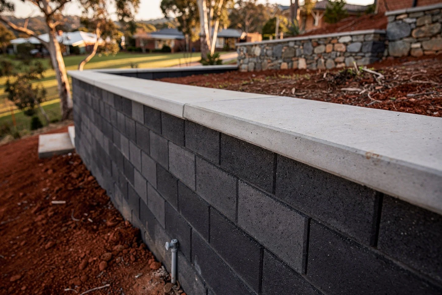 A finished core-filled besser retaining wall with a poured concrete cap, courses dead level and mortar joints raked clean